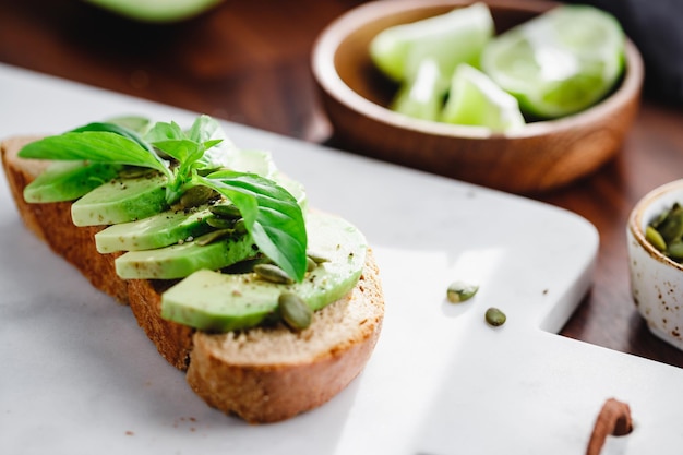 Tostadas de aguacate con pepitas y albahaca fresca sobre una tabla de cortar de mármol blanco Concepto de alimentación saludable para cocinar en casa