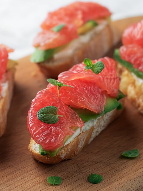 Tostadas con aguacate, queso blando, pomelo en una mesa de madera