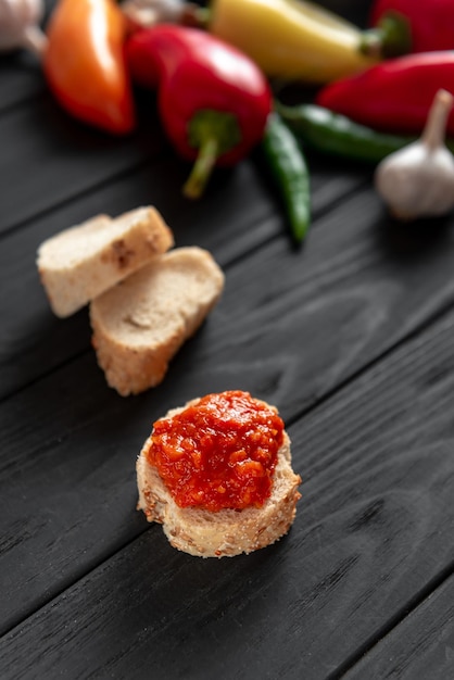 Tostadas con ajika sobre un fondo oscuro de madera, los ingredientes están uno al lado del otro