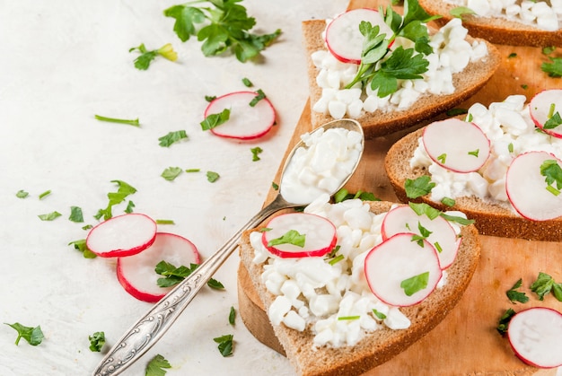 Tostadas caseras con requesón, rábano y perejil en mesa blanca, espacio de copia