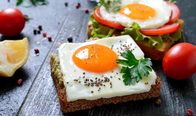 Tostadas de centeno con puré de aguacate, huevo frito, tomate fresco, hierbas. Desayuno sabroso Nutrición apropiada. Sandwich con huevo.