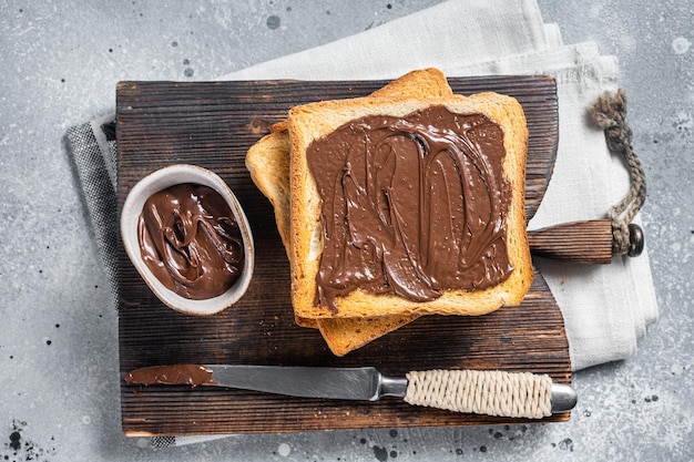 Tostadas con chocolate y avellanas para untar sobre tabla de madera Fondo gris Vista superior