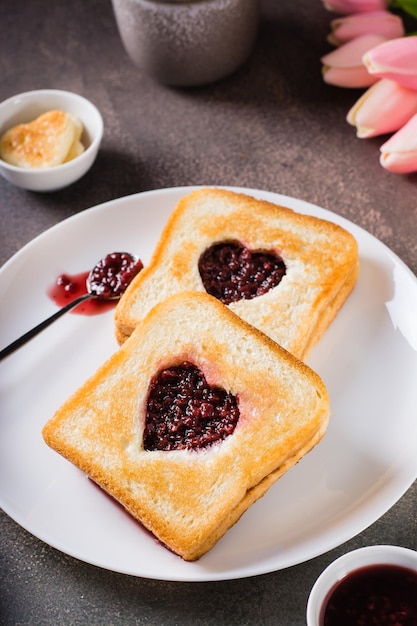 Tostadas con un corazón lleno de mermelada de frambuesa en un plato Desayuno para una pareja Vista vertical