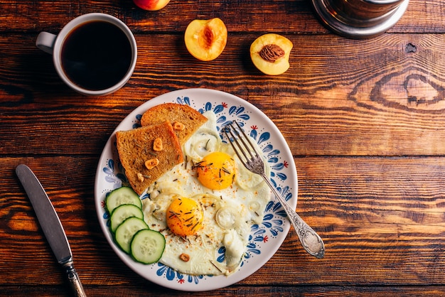Tostadas de desayuno con huevos fritos con verduras en un plato y una taza de café con frutas sobre la mesa de madera oscura, vista superior. Concepto de comida sana.