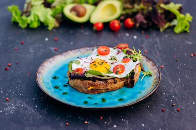 Tostadas francesas con ensalada de tocino de huevo frito y tomates servidos en un plato azul Concepto de desayuno sabroso