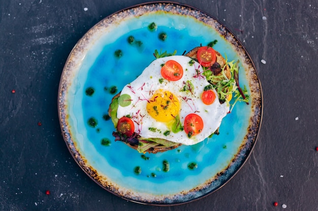 Tostadas francesas con ensalada de tocino de huevo frito y tomates servidos en un plato azul Concepto de desayuno sabroso