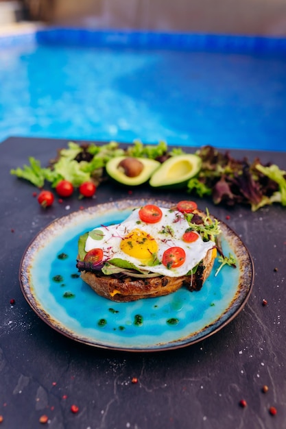 Tostadas francesas con ensalada de tocino de huevo frito y tomates servidos en un plato azul Concepto de desayuno sabroso