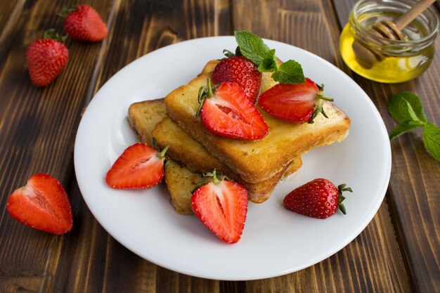 Tostadas francesas con fresas y miel en la placa blanca.