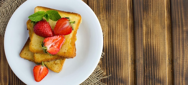 Tostadas francesas con fresas y miel en el plato blanco sobre el fondo rústico de madera Vista superior Espacio de copia