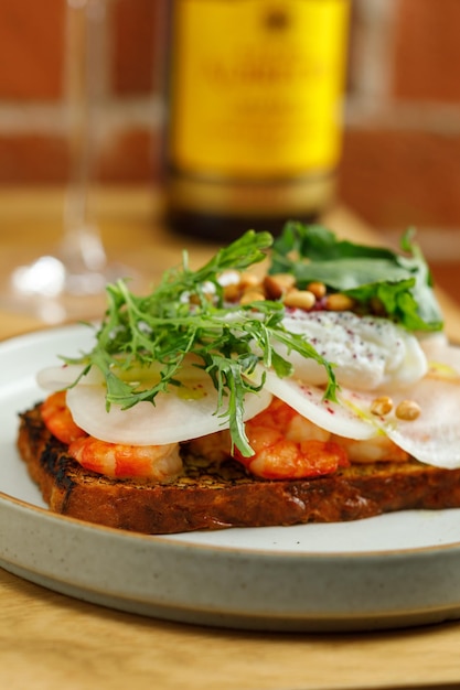 Foto tostadas con gambas a la parrilla y verduras, huevo escalfado y hierbas en la parte superior servido en el restaurante botella de vino y copa en el fondo