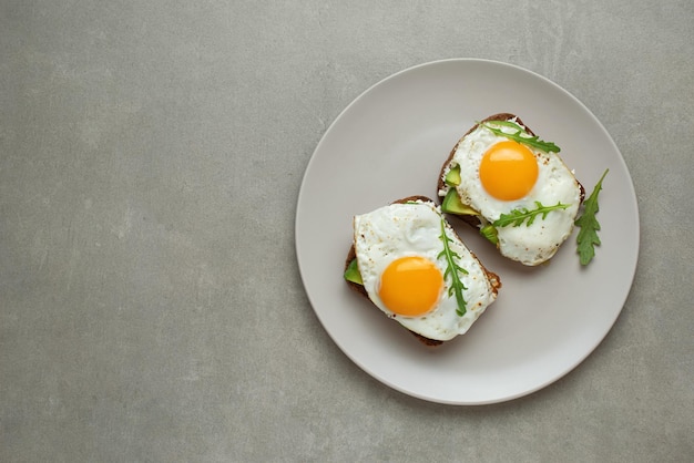 Tostadas con huevo y aguacate sobre un fondo gris en un plato desayuno saludable