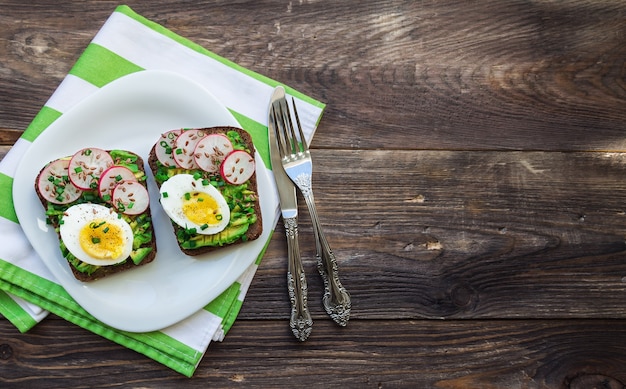 Tostadas con huevos de aguacate, rábano, cebolla verde y semillas de lino sobre fondo de madera rústica vista superior