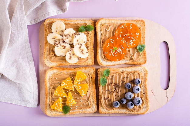 Tostadas con mantequilla de maní, frutas, bayas, semillas de lino y semillas de sésamo en una tabla de cortar Vista superior