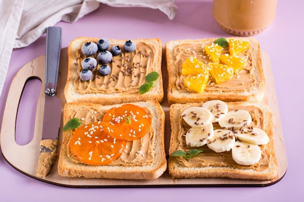 Tostadas con mantequilla de maní, plátano, caqui, naranja, semillas de lino y semillas de sésamo en una tabla para cortar