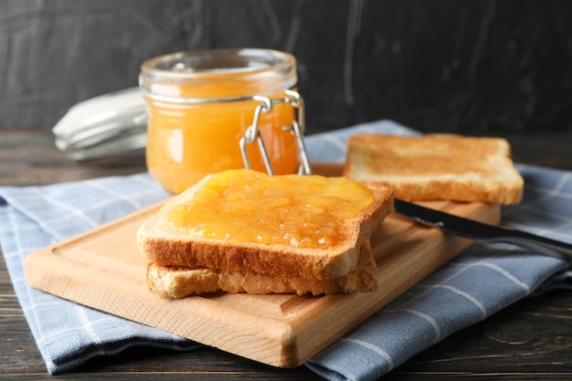 Foto tostadas con mermelada de albaricoque, tabla, toalla y jarra sobre madera, cerrar