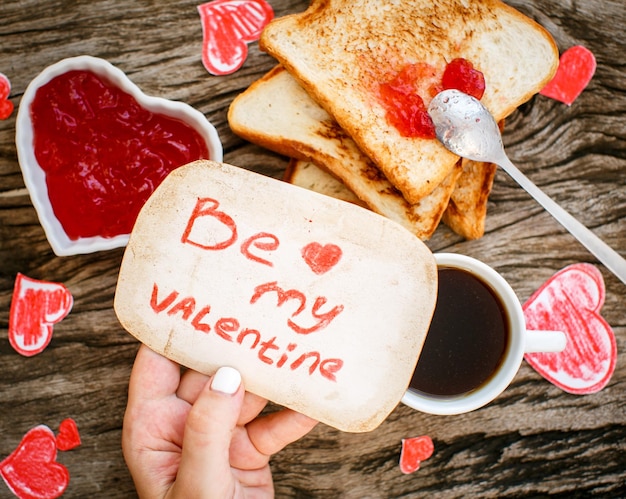 Tostadas con mermelada de fresa Tarjeta de mensaje blanca Be My Valentine con café en las manos Día de San Valentín