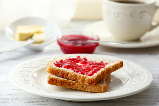 Tostadas con mermelada en plato con taza de té sobre fondo claro