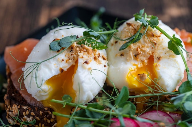 Tostadas de pan, huevos escalfados, microvegetales de guisantes de salmón y verduras frescas en un plato a la hora del desayuno en la cafetería