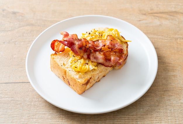 Tostadas de pan con huevos revueltos y tocino en la placa blanca.