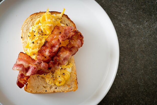 Tostadas de pan con huevos revueltos y tocino en la placa blanca.