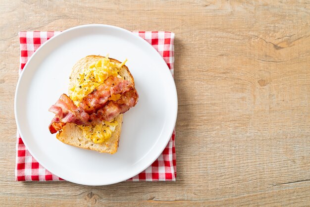 Tostadas de pan con huevos revueltos y tocino en la placa blanca.