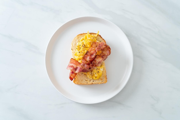 Tostadas de pan con huevos revueltos y tocino en la placa blanca.