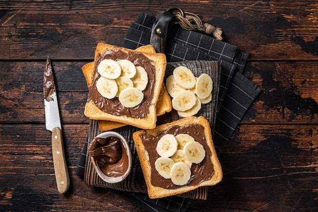 Tostadas de pan con plátanos y crema de chocolate sobre tabla de madera Fondo de madera Vista superior