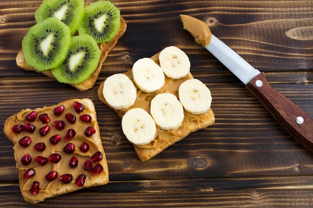 Tostadas con pasta de maní, fruta y cuchillo sobre la superficie de madera