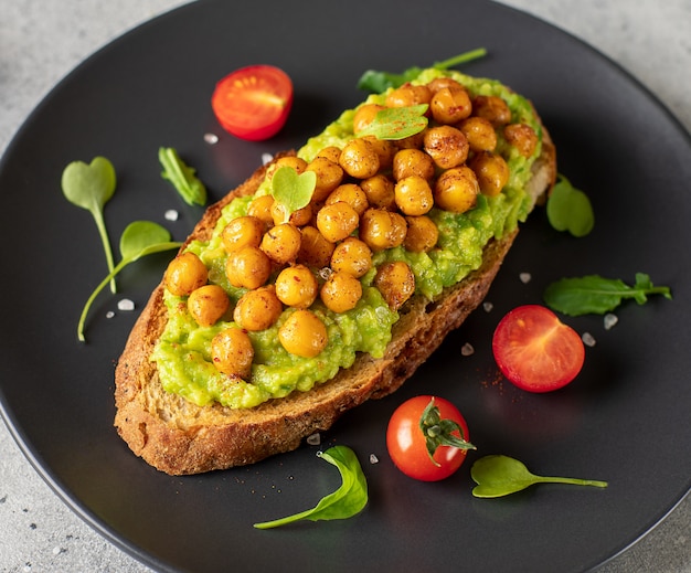 Tostadas con puré de aguacate, garbanzos asados, tomates cherry, hierbas en un plato oscuro concepto de comida sana close-up