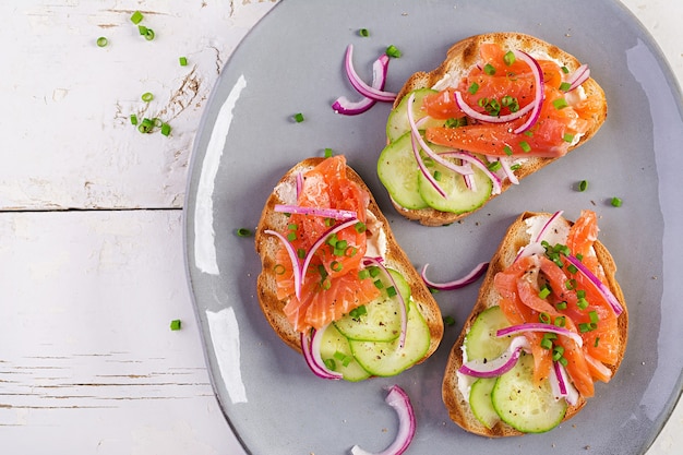 Tostadas con queso crema, salmón ahumado, pepino y cebolla roja sobre mesa de madera rústica. Sándwiches abiertos. Cuidado saludable, concepto de súper comida. Vista superior, arriba