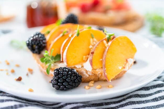 Tostadas de ricotta de melocotón adornadas con moras en un plato blanco.