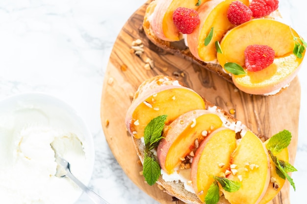 Tostadas de ricotta de melocotón adornadas con nueces, menta fresca y frambuesas en una tabla de cortar de madera.