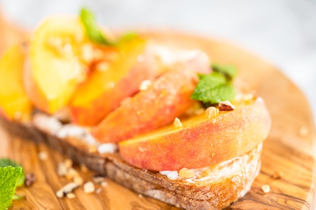 Tostadas de ricotta de melocotón adornadas con nueces y menta fresca en una tabla de cortar de madera.