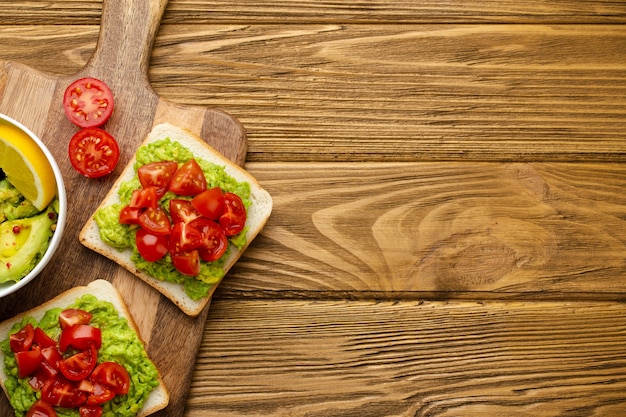 Tostadas saludables con aguacate aplastado y tomates frescos picados en la tabla de cortar sobre fondo marrón rústico de madera. Sándwiches vegetarianos, bocadillos saludables para la dieta, alimentación limpia. Vista superior, espacio de copia