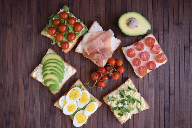 Tostadas saludables para el desayuno con aguacate, huevos, tomates, rúcula, etc.