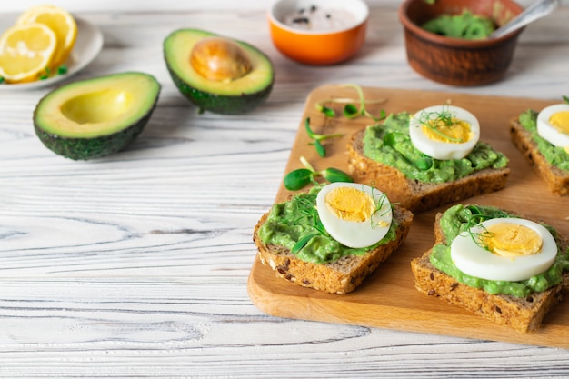 Tostadas saludables con pan integral, aguacate y huevo cocido sobre tabla de madera.