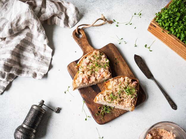 Tostadas saludables con paté de salmón y brotes verdes frescos en pan sin levadura sobre tabla para cortar madera