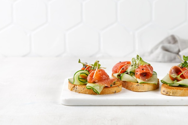 Tostadas saludables con pepinos en rodajas de salmón y microvegetales Aperitivos de bocadillos Bruschetta Sándwiches en pizarra blanca y fondo blanco