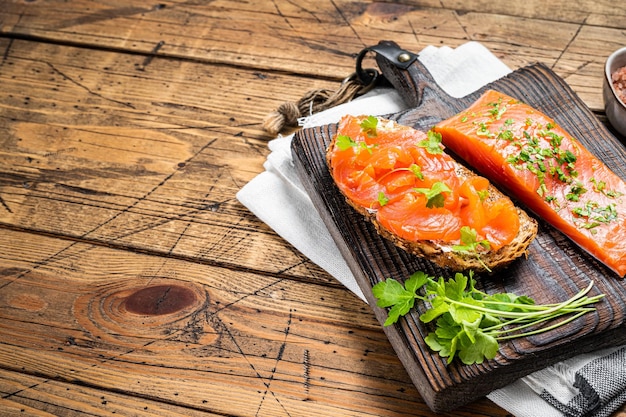 Tostadas de sándwich con hierbas de filete de salmón salado sobre una tabla de madera Fondo de madera Vista superior Espacio de copia