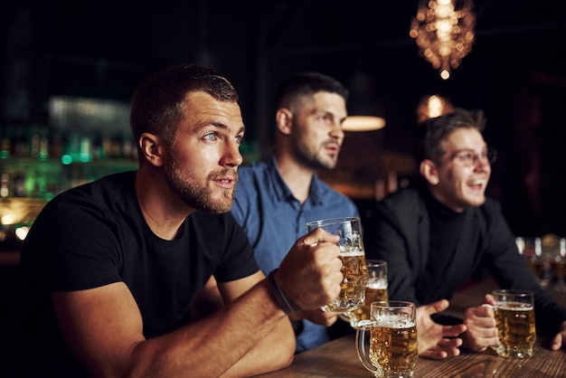 Totalmente concentrado. Três fãs de esportes em um bar assistindo futebol. Com cerveja nas mãos.