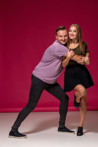 Foto totalmente enamorado. longitud total de la hermosa joven pareja abrazándose y sonriendo mientras está de pie contra el fondo de borgoña