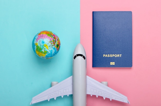 Tourismus- und Reisekonzept. Auswanderung. Globus-, Pass- und Passagierflugzeugfigur auf rosa blauer Pastellwand Draufsicht. Flach liegen