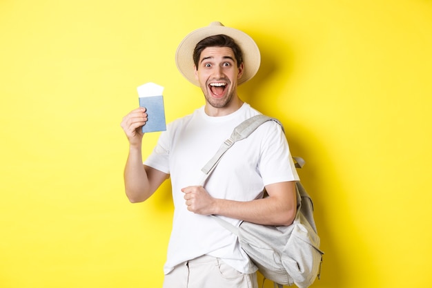 Tourismus und Urlaub. Aufgeregter Kerl Tourist, der auf Urlaubsreise geht, Reisepass mit Tickets zeigt und Rucksack hält, auf gelbem Hintergrund steht.
