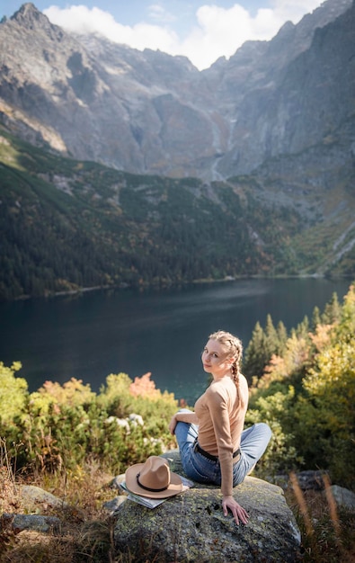 Tourist der jungen Frau, der auf dem Berggipfel und den schönen Bergen sitzt