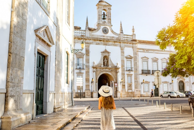 Tourist der jungen Frau, der auf dem Stadttorhintergrund in der Stadt Faro im Süden Portugals steht?