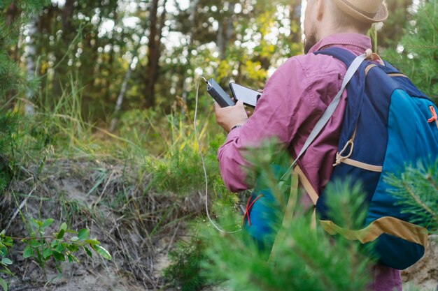 Tourist hält ein Smartphone mit einem tragbaren Ladegerät in den Händen. Mann mit Powerbank lädt das Telefon vor der Kulisse von Natur und Wald auf.