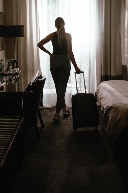 Tourist mit Koffer ließ sich in einem Luxuszimmer nieder und genießt die Aussicht vom Fenster