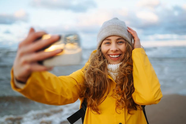 Tourist mit Telefon Selfie-Zeit Tourist in gelber Jacke posiert am Meer bei Sonnenuntergang Reisen