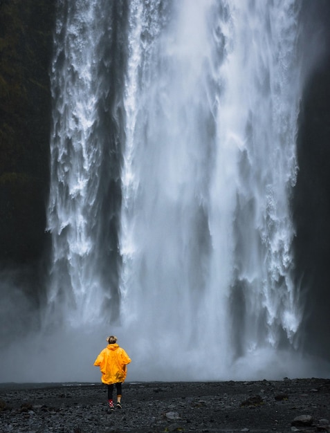 Touristen, die einen gelben Regenmantel tragen, gehen zum Skogafoss-Wasserfall in Island