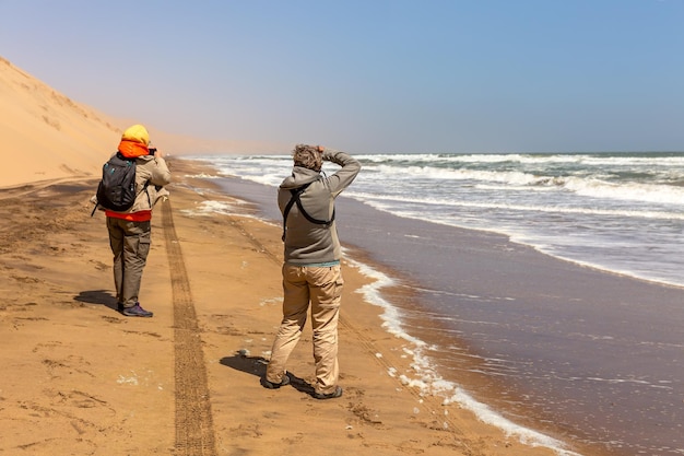 Touristen fotografieren die Dünen und das Meer in Sandwich Harbor. Namibia